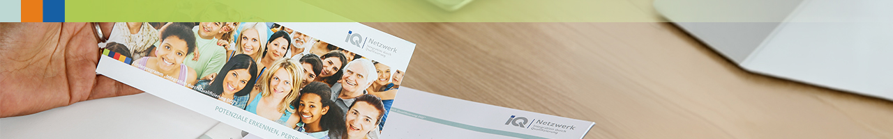 Hand hält Flyer mit Gruppenfoto von verschiedenen Menschen.